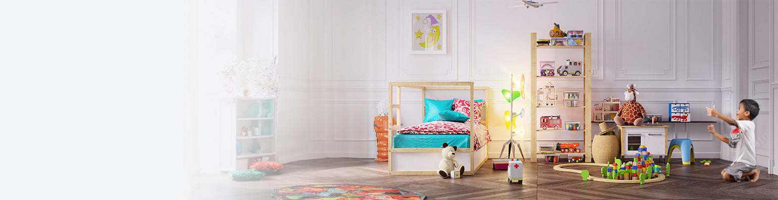 Ein Junge sitzt in einem Kinderzimmer mit viel Spielzeug, einem Bett, Kuscheltieren und einer Lampe.