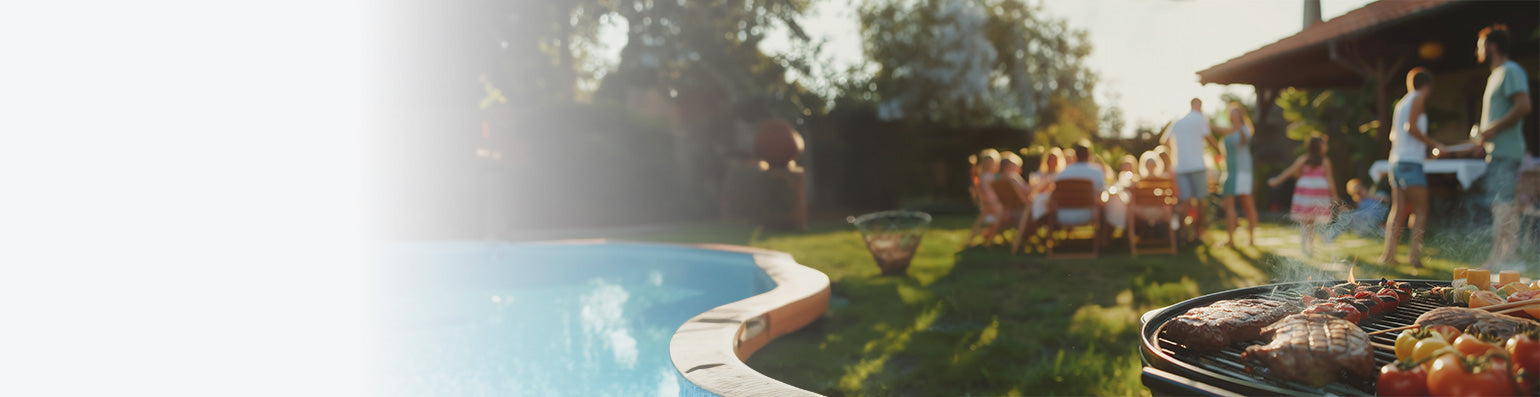 Ein gefüllter Kugelgrill steht an einem Pool, dahinter sitzen Menschen im Garten an einem Tisch, daneben ein Feuerkorb.