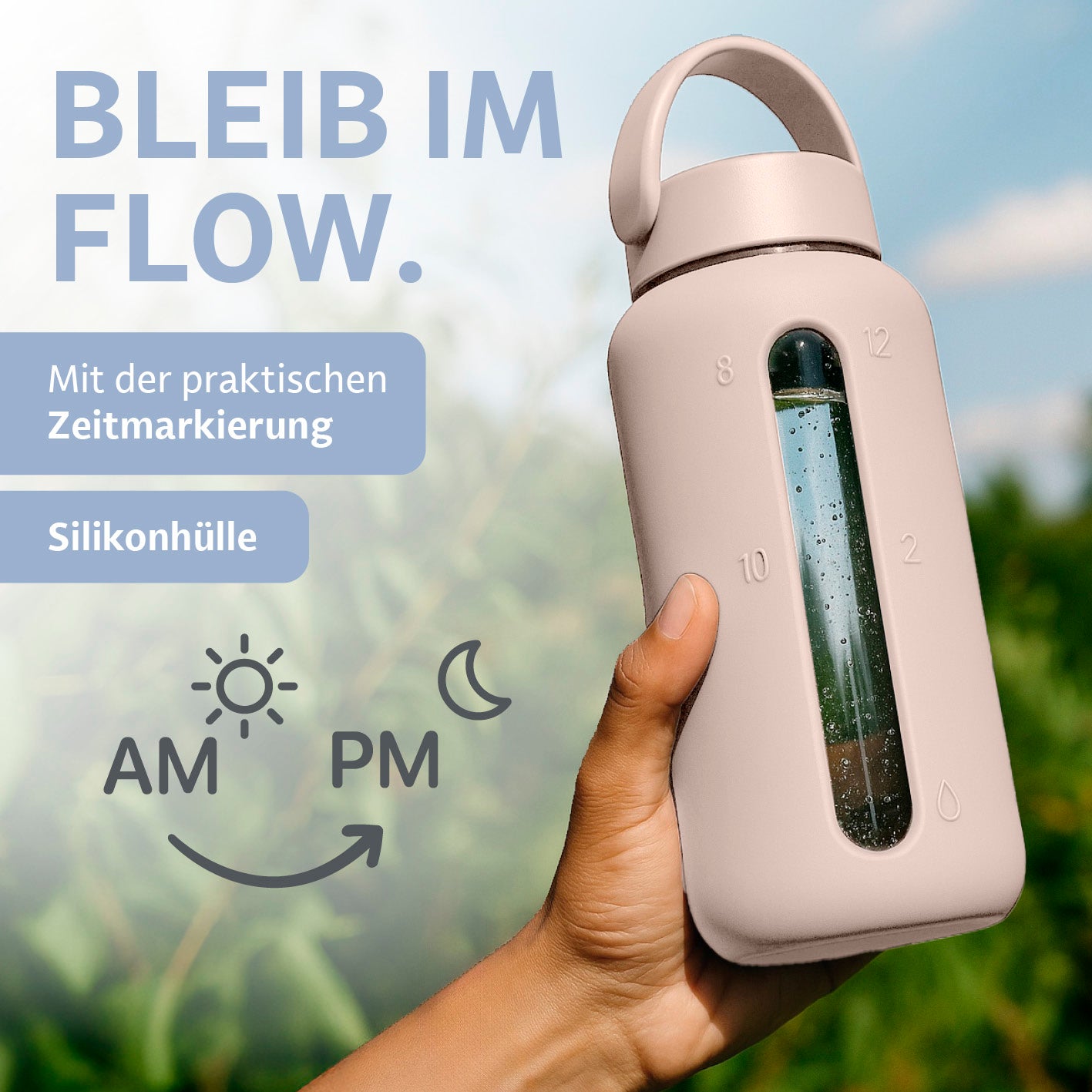 Hand hält Glas-Trinkflasche – Creme mit Silikonhülle und Zeitmarkierung von 8 bis 20 Uhr vor unscharfem Hintergrund draußen.