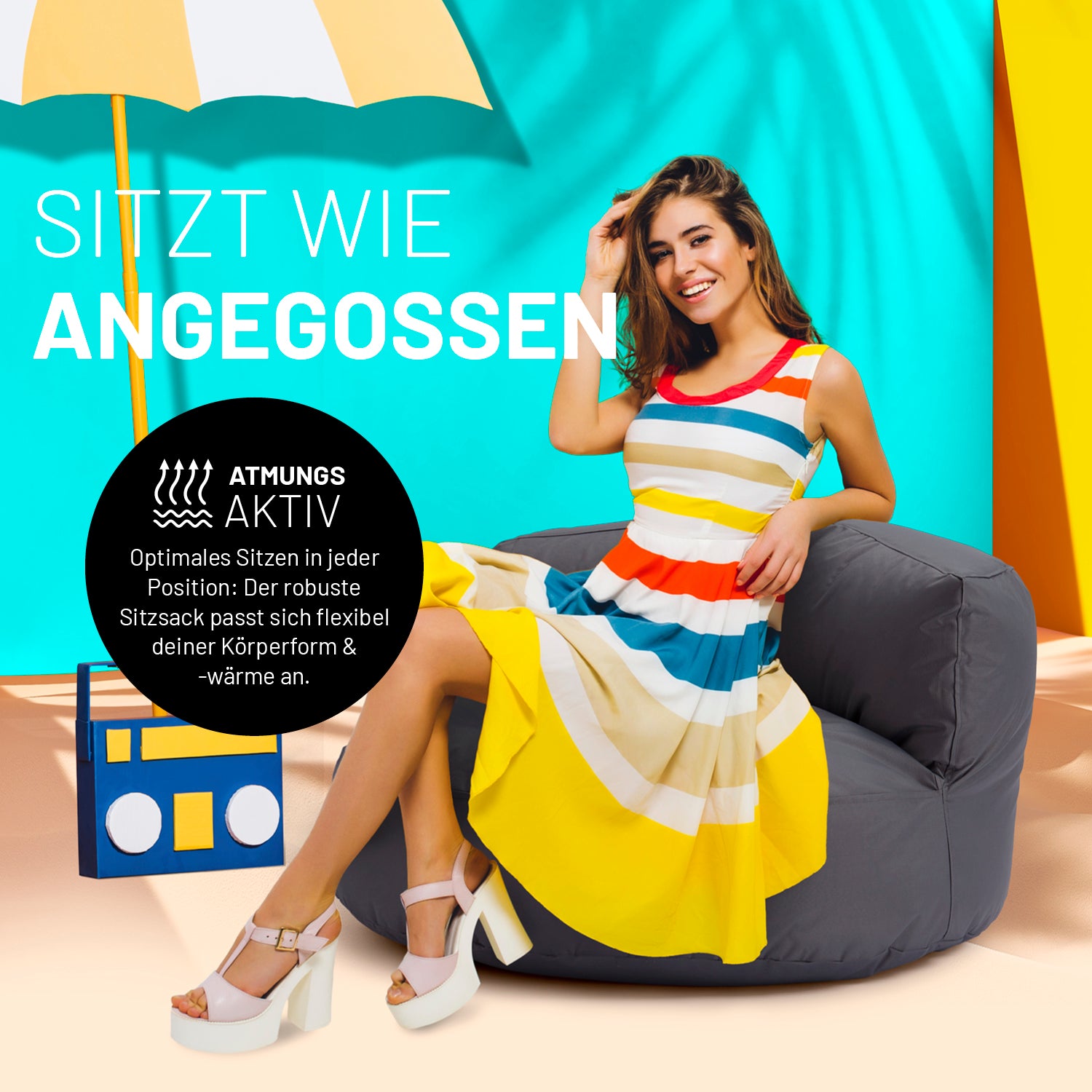 Frau sitzt entspannt auf Sitzsack Lounge (320 L) - indoor & outdoor - Anthrazit vor buntem Hintergrund mit Sonnenschirm.