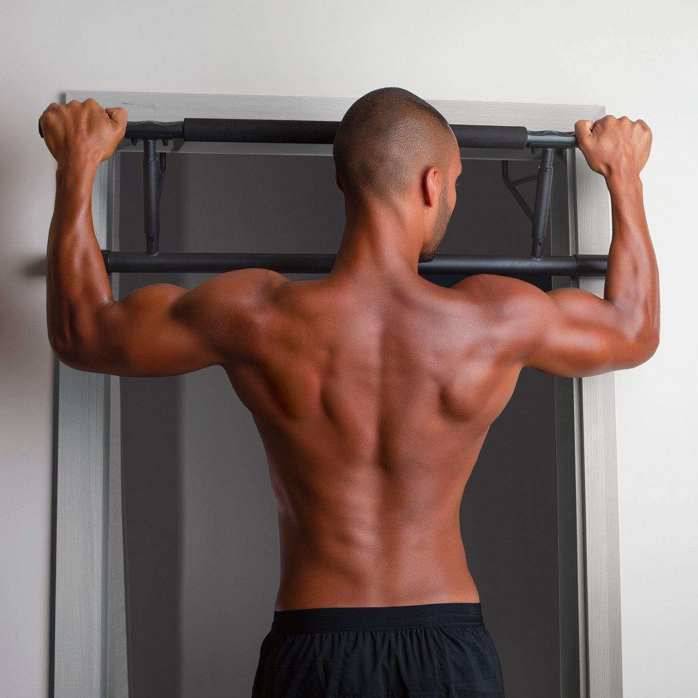 Mann trainiert Rückenmuskulatur mit Klimmzugstange für den Türrahmen, einfach montiert und belastbar bis 130 kg.