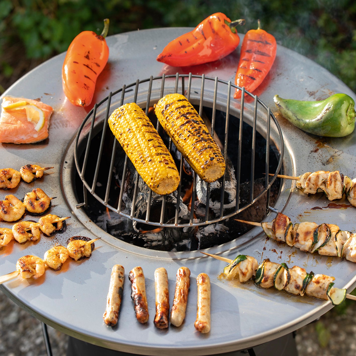 Holzkohlegrill mit Grillrost und Grillplatte mit gegrilltem Gemüse, Fleisch und Schalentiere für vielseitiges Grillvergnügen im Tischgrillformat.