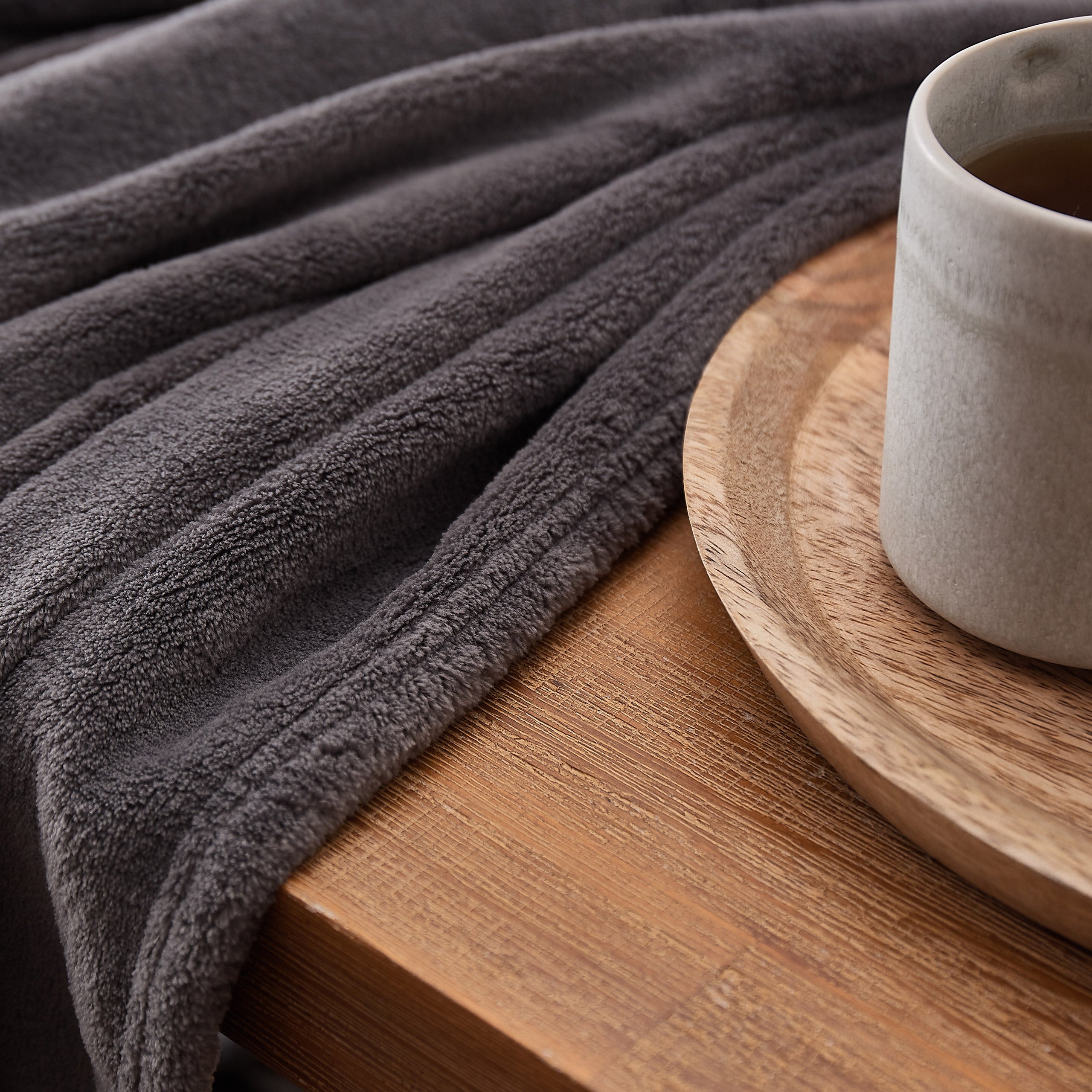 Kuscheldecke - 150x200 cm - Sofadecke & Tagesdecke - Grau aus weichem Coral-Fleece auf Holz mit grauem Design und Tasse.