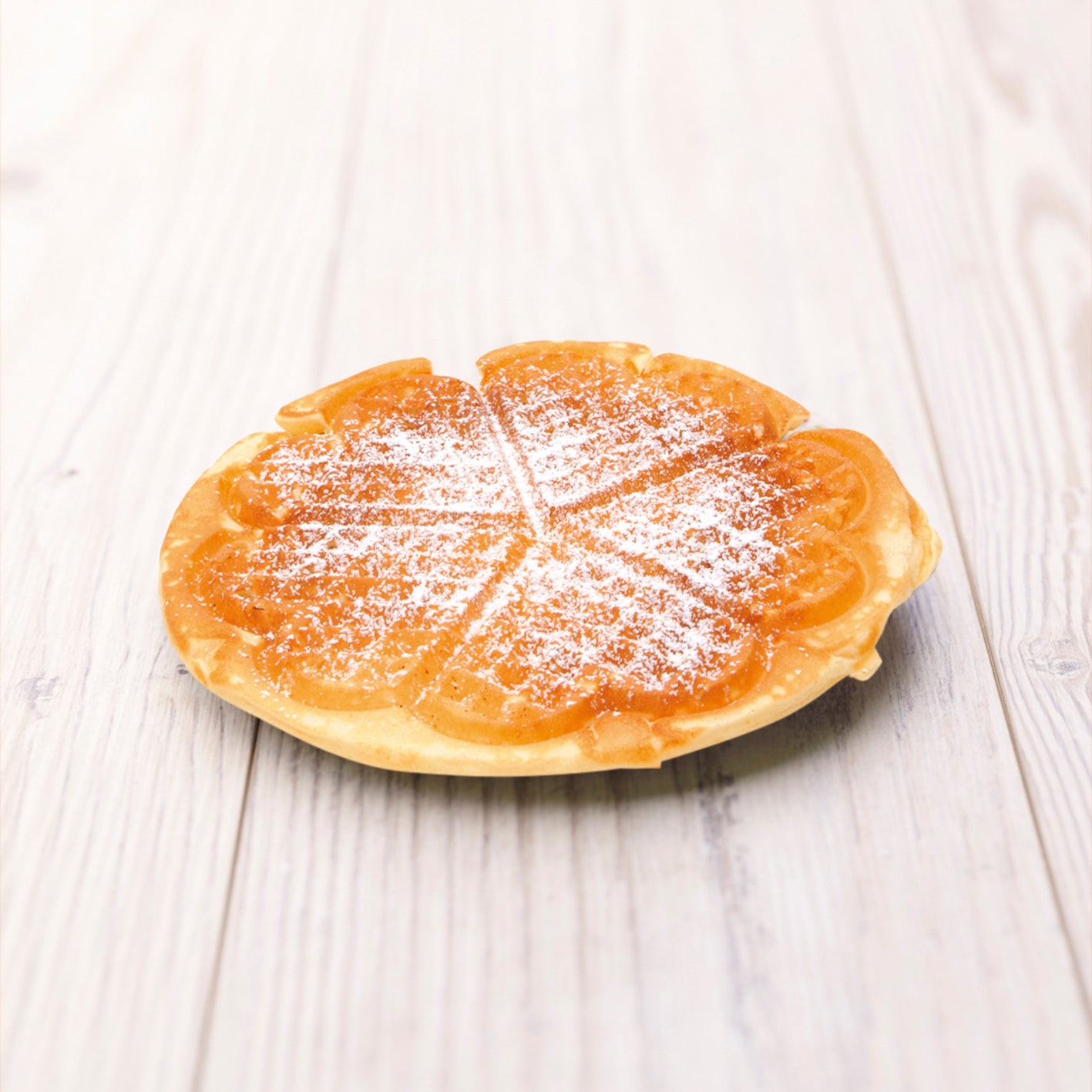Waffel mit Puderzucker bestäubt auf hellem Holztisch, passend zum Rezeptbuch inkl. Messbecher-Set Band 1 für Kinder.