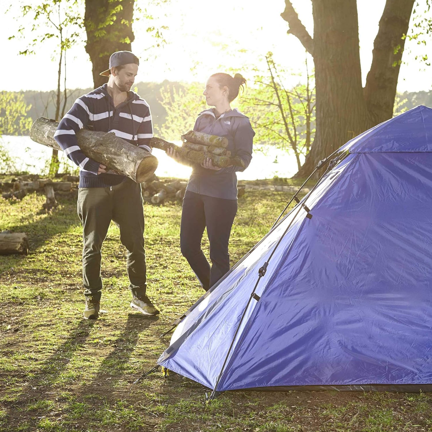 Pop Up Familienzelt Wurfzelt 3 Personen Zelt Blau im Wald, zwei Personen tragen Holz, ideal fürs Camping und Outdoor-Aktivitäten.