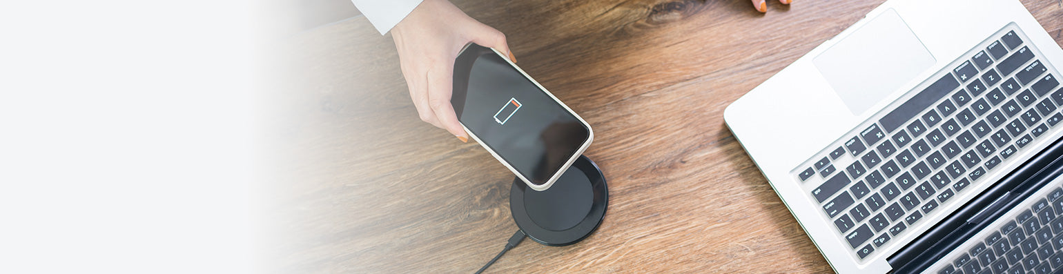 Ein Handy mit leerem Akku wird über eine Ladestation gehalten, daneben ein Laptop.