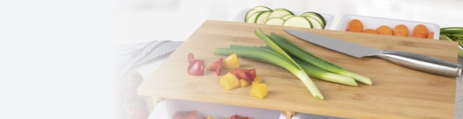 Frühlingszwiebeln und Paprika liegen auf einem Holzbrett, daneben ein Messer.