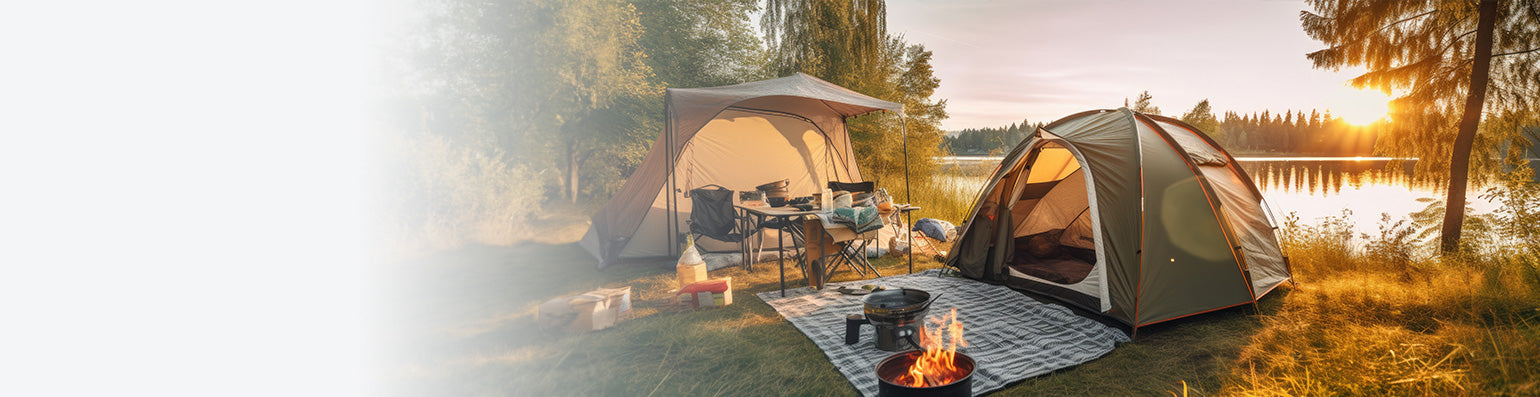 Zwei Zelte im Sonnenuntergang an einem See, eine Feuerstelle aufgebaut und eine ausgebreitete Decke.