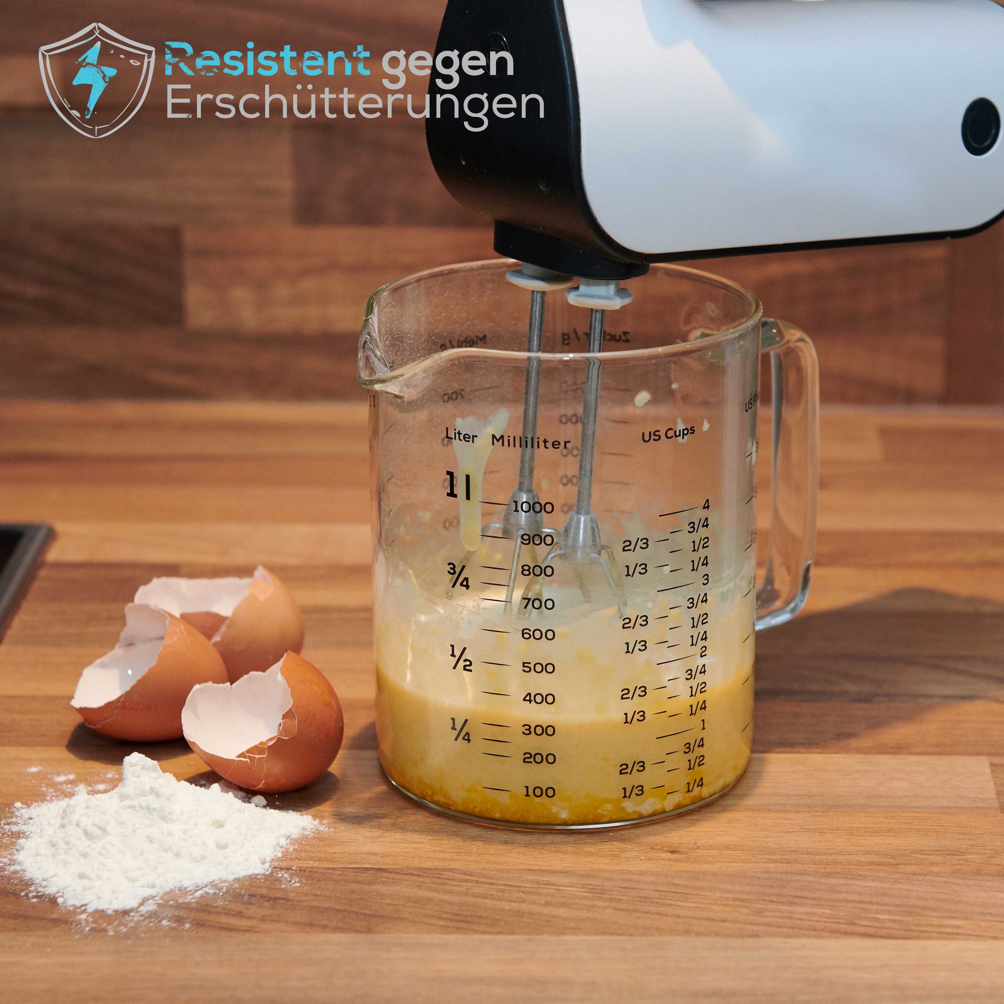 Messbecher - Glas - 1 L & 500 ml - 2er Set mit integrierter Skala beim Rühren von Zutaten, daneben Eierschalen und Mehl auf Holzarbeitsfläche.