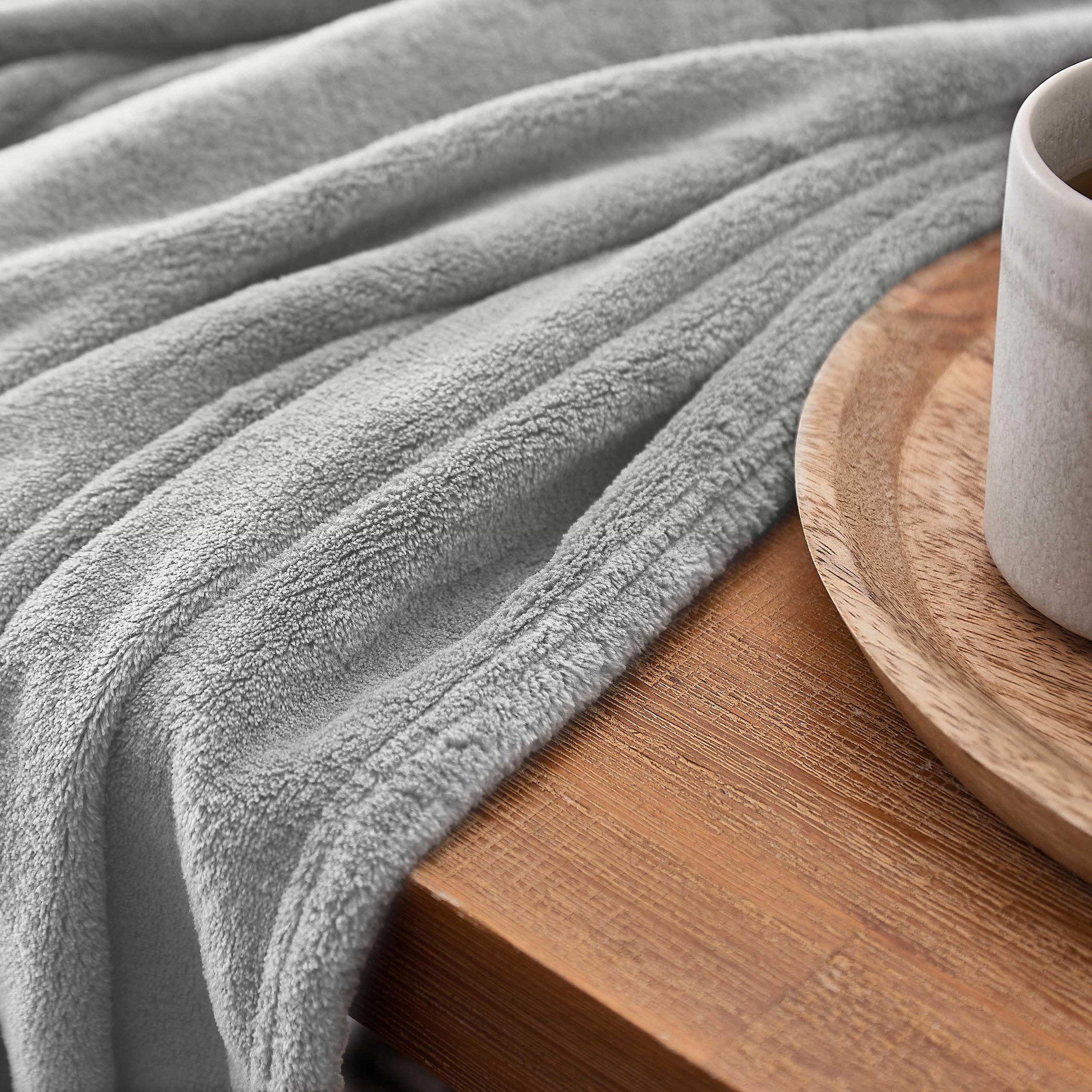 Kuscheldecke - 150x200cm - Sofadecke & Tagesdecke - Hellgrau aus weichem Coral-Fleece auf Holztisch mit Tasse.