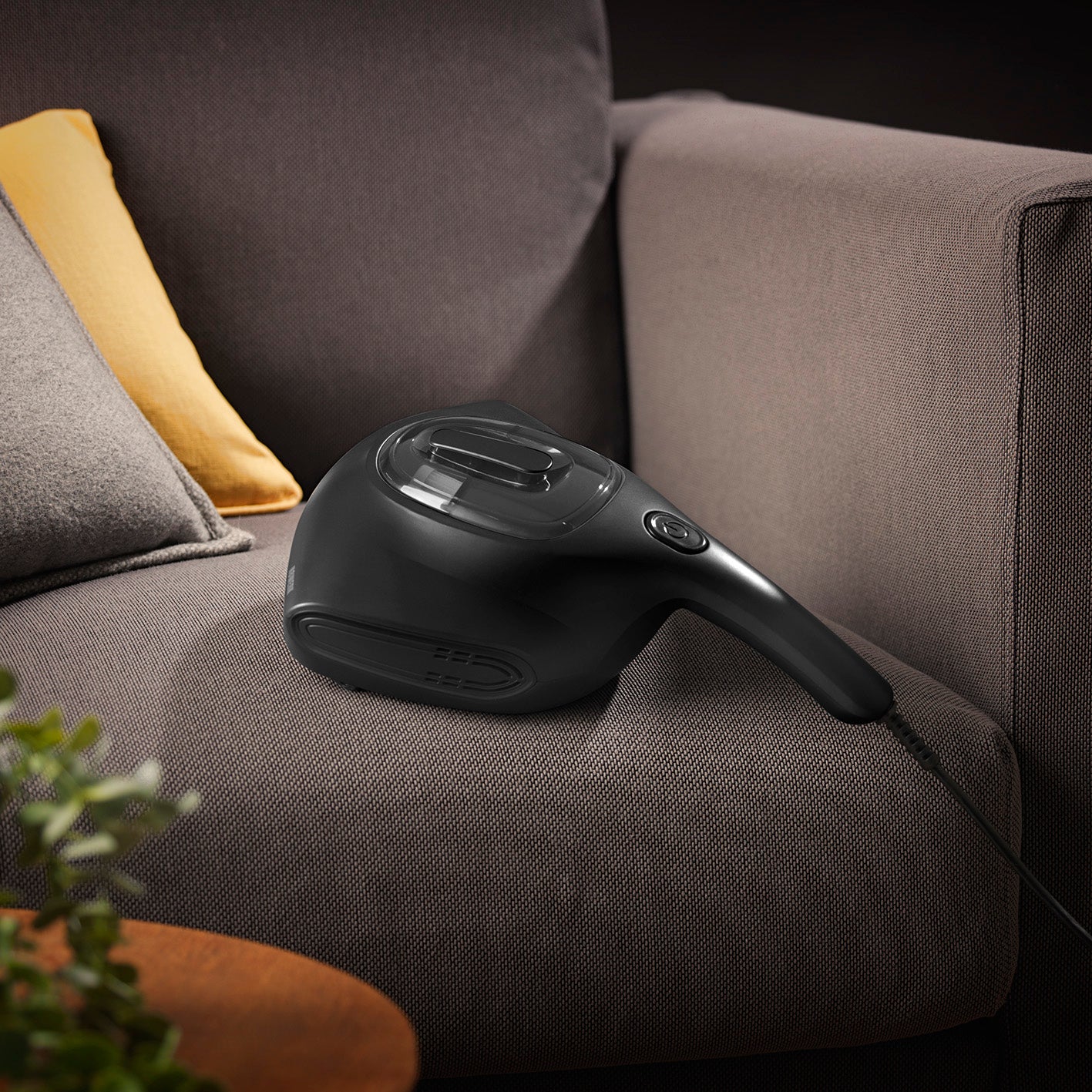 Milbensauger Midnight Black Edition auf grauem Sofa, mit HEPA-Filter und UV-C Licht zur hygienischen Reinigung von Textilien.