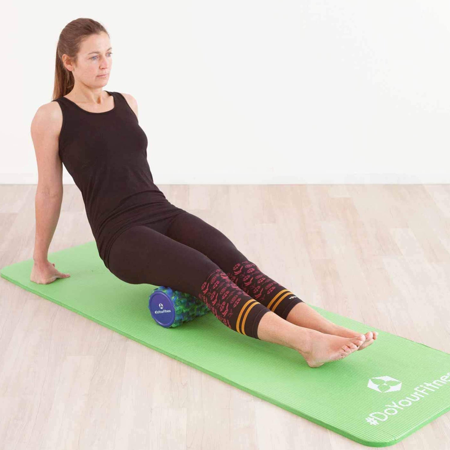 Frau nutzt Faszienrolle Anila eckig 45x15 cm Schwarz/Rot zur Selbstmassage der Waden auf grüner Yogamatte.