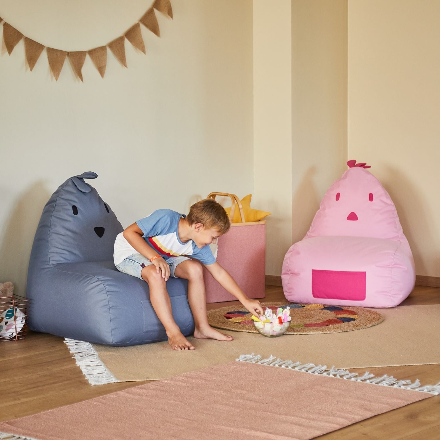 Gemütliche Kinderecke mit bunten LUMALAND Sitzsäcken in Tierform, Teppichen und einem Jungen beim Spielen mit Stofftieren.